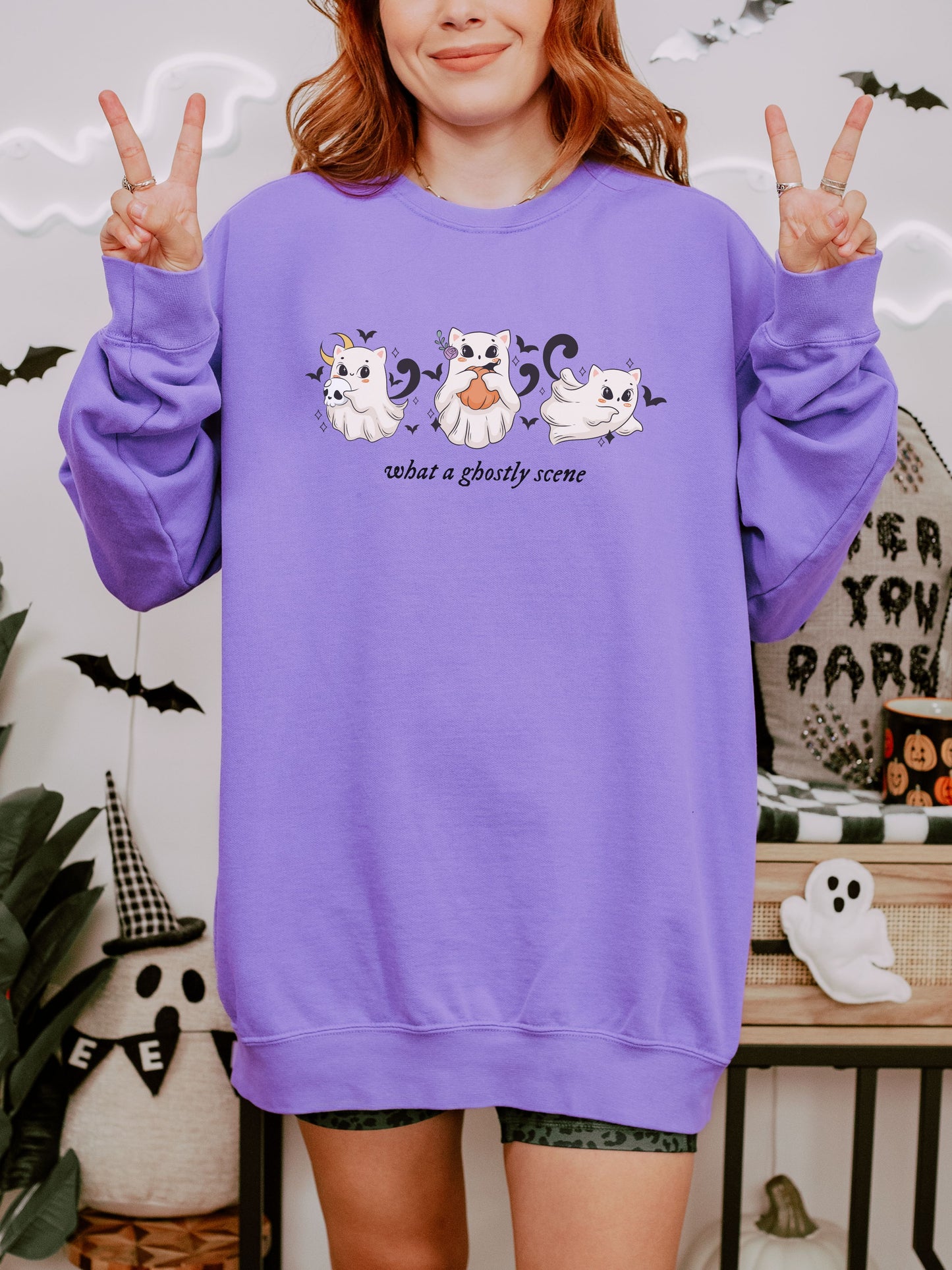 Person wearing a purple sweatshirt with Halloween-themed design, making peace signs.