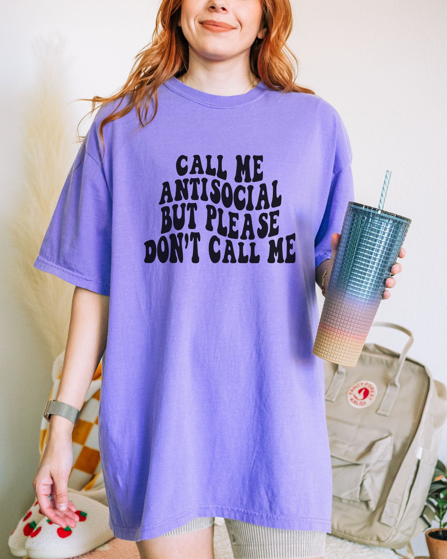 Person wearing a purple t-shirt with text, holding a blue and pink gradient cup.