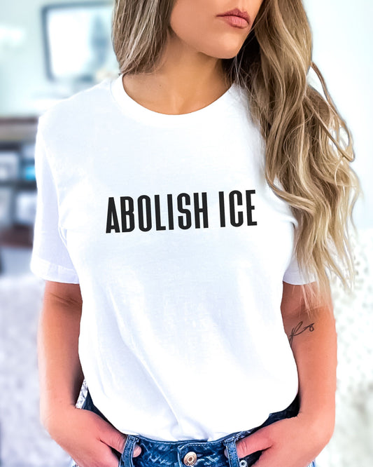 Person wearing a white t-shirt with 'ABOLISH ICE' text.