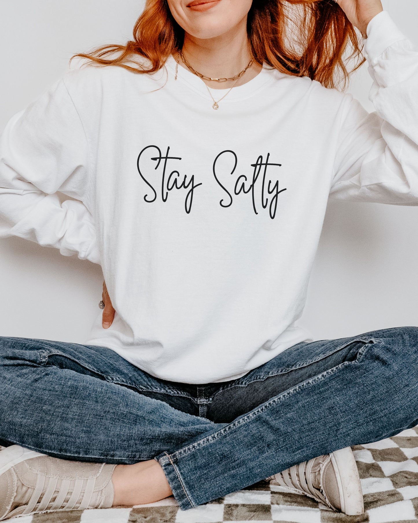 Person wearing a white sweatshirt with 'Stay Salty' text, sitting on a checkered blanket.