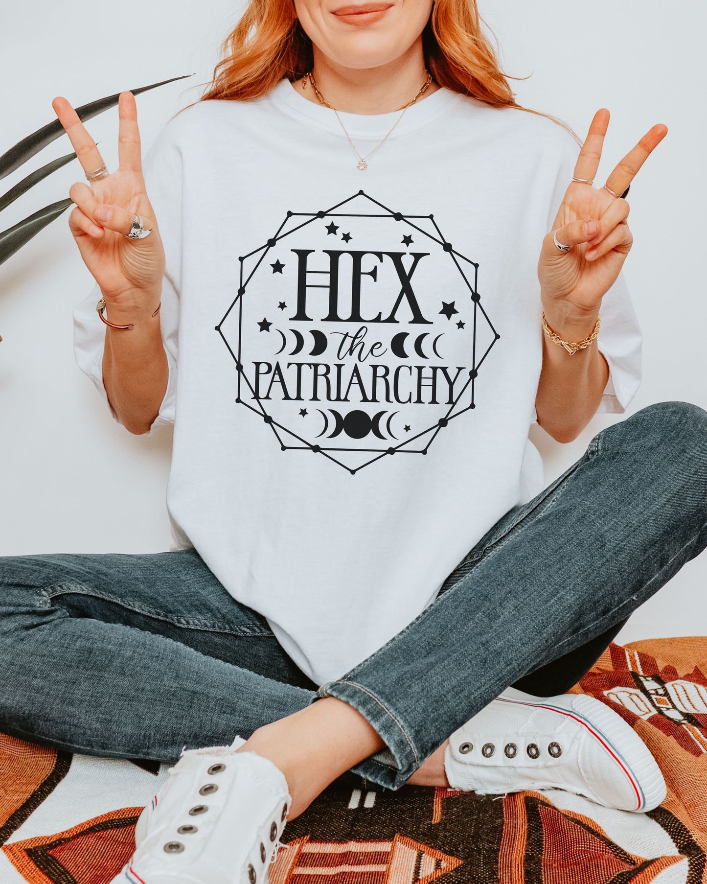 Person wearing a white sweatshirt with 'Hex the Patriarchy' text, sitting on a patterned rug.