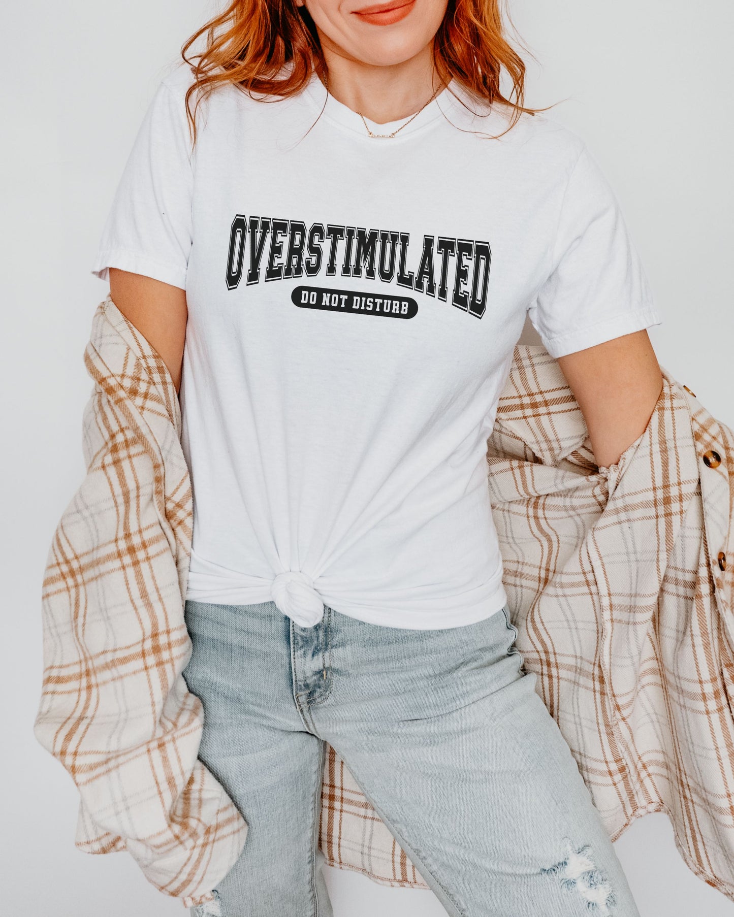Person wearing a white t-shirt with 'OVERSTIMULATED DO NOT DISTURB' text, standing against a plain background.