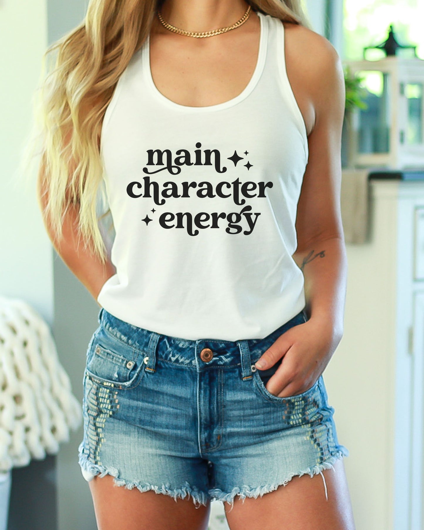 Person wearing a white tank top with 'main character energy' text and denim shorts.