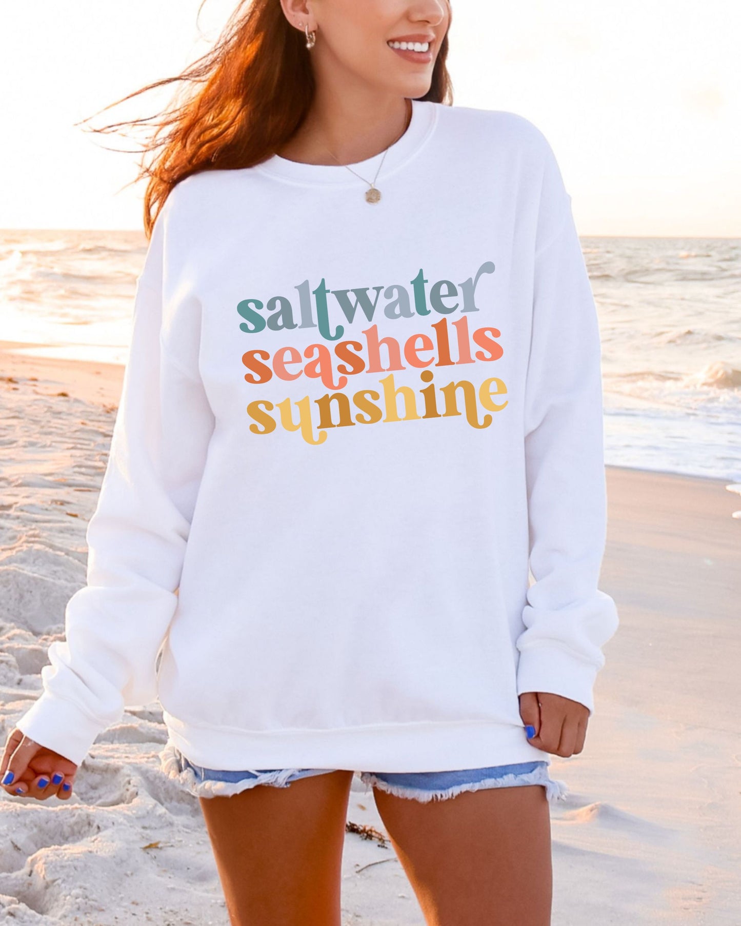Person wearing a white sweatshirt with colorful text on a beach