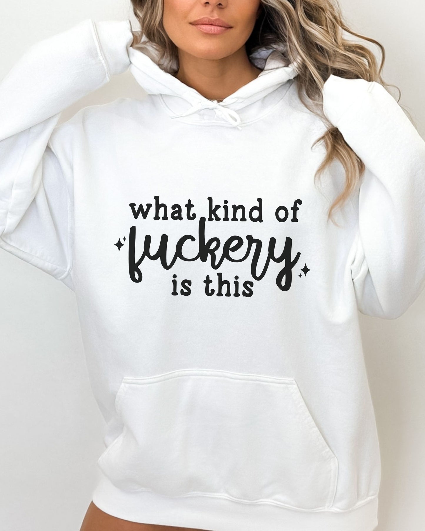 White hoodie with text 'what kind of fuckery is this' worn by a person on a plain background