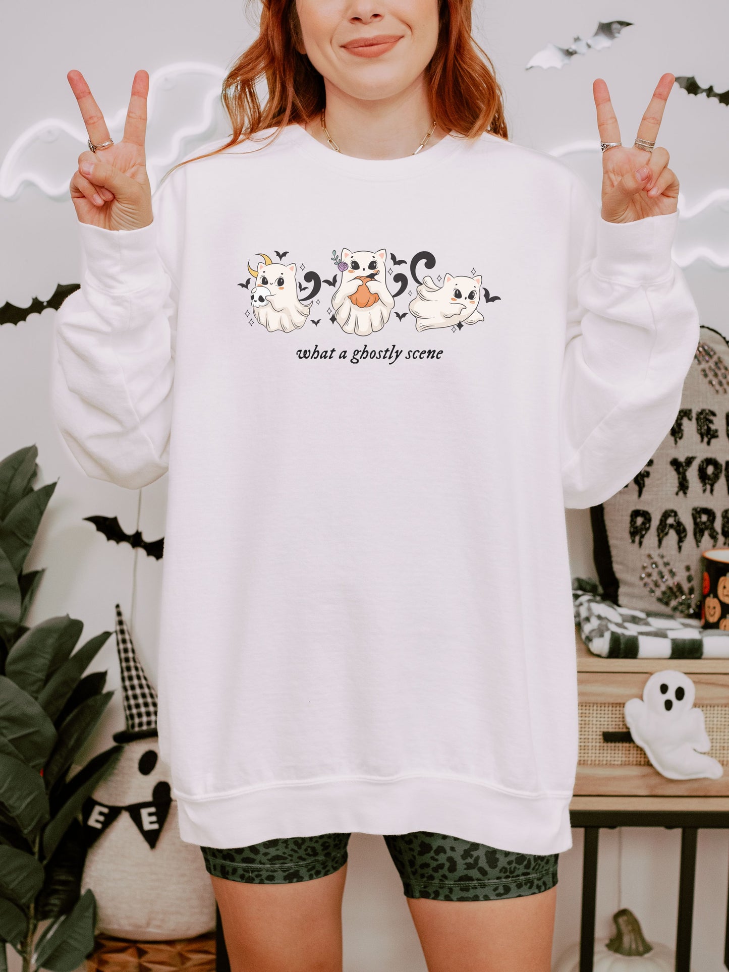 Person wearing a white sweatshirt with ghost designs and text, making peace signs.