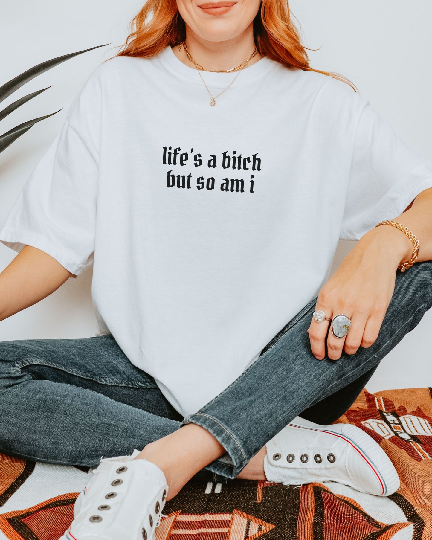 Person wearing a white sweatshirt with text, sitting on a patterned rug.