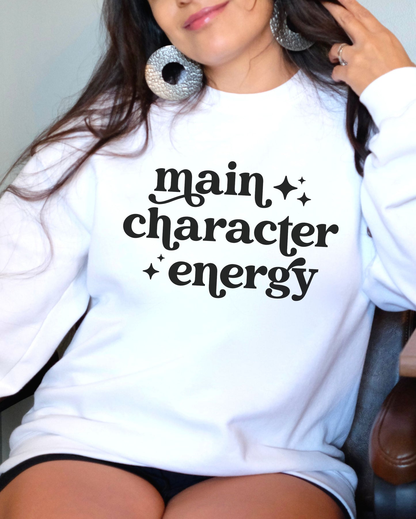 Person wearing a white sweatshirt with 'main character energy' text