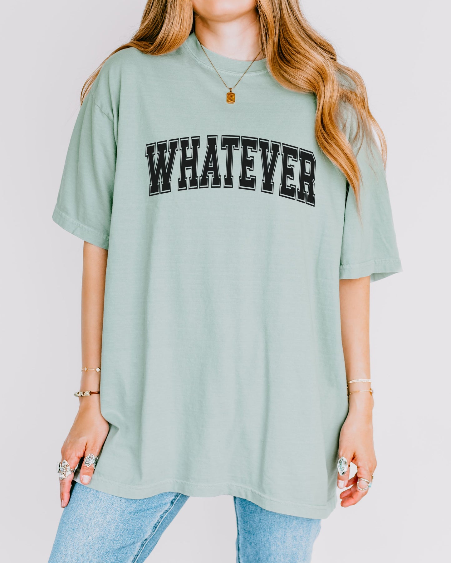 Person wearing a light green t-shirt with 'WHATEVER' printed on it against a plain background
