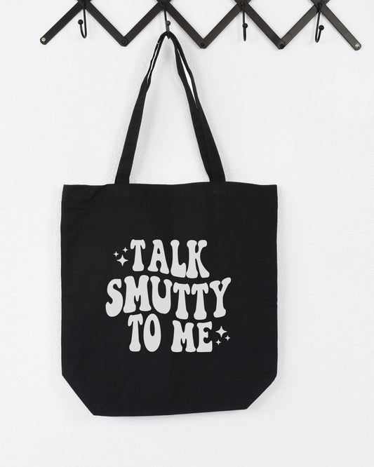 Black tote bag with 'Talk Smutty To Me' text on a white background