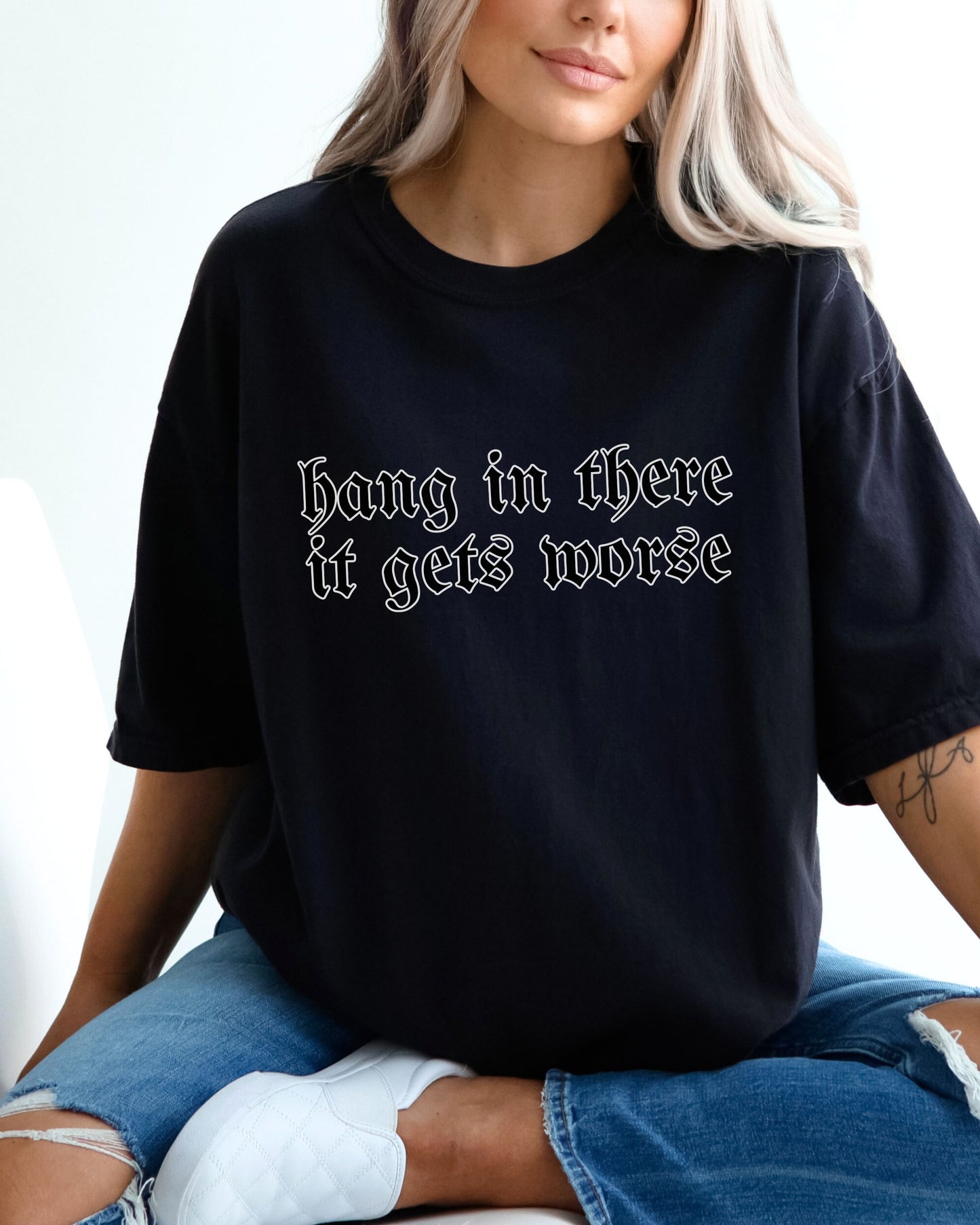 Person wearing a black t-shirt with text 'Hang in there it gets worse' on a plain background