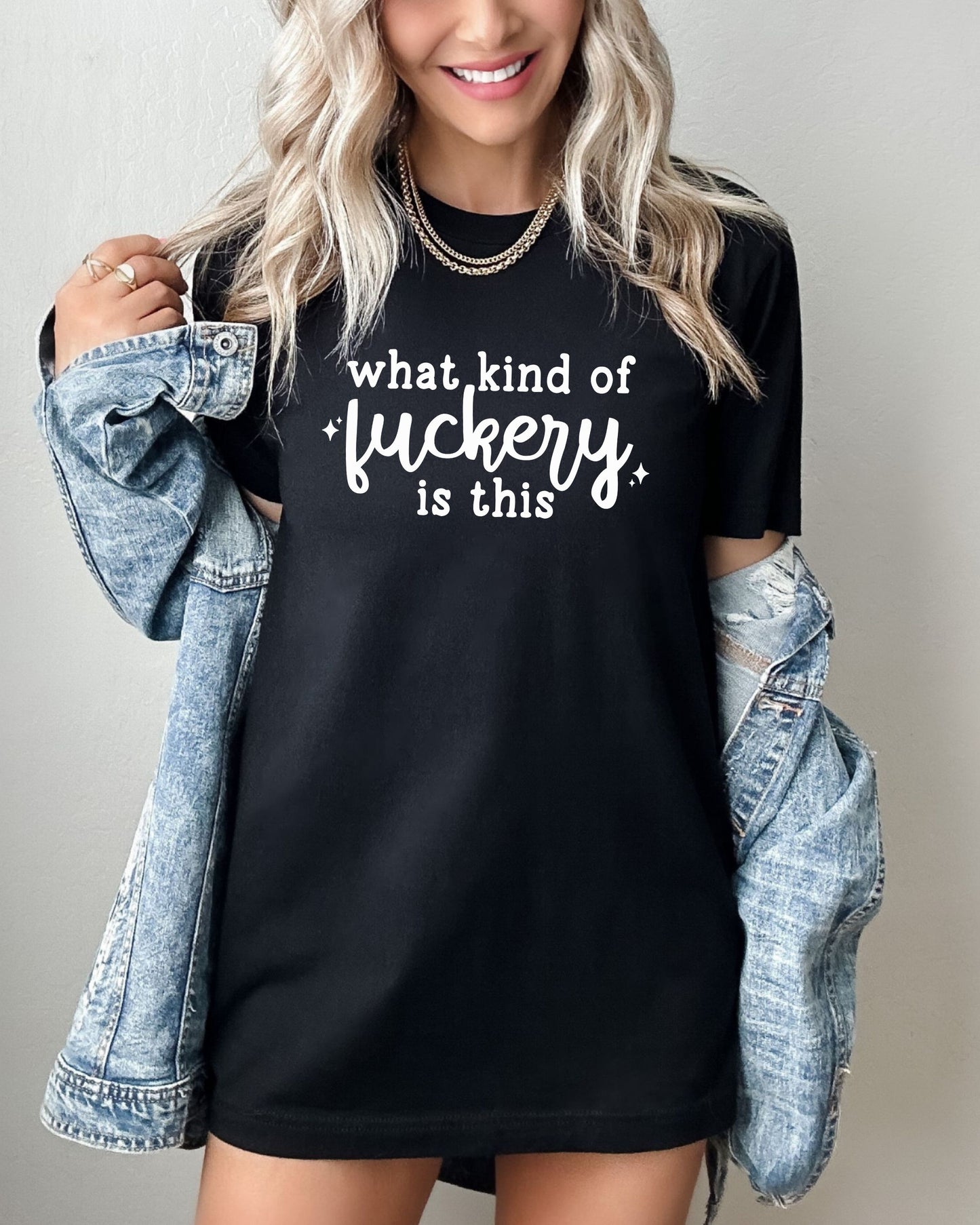 Person wearing a black t-shirt with text and a denim jacket on a plain background
