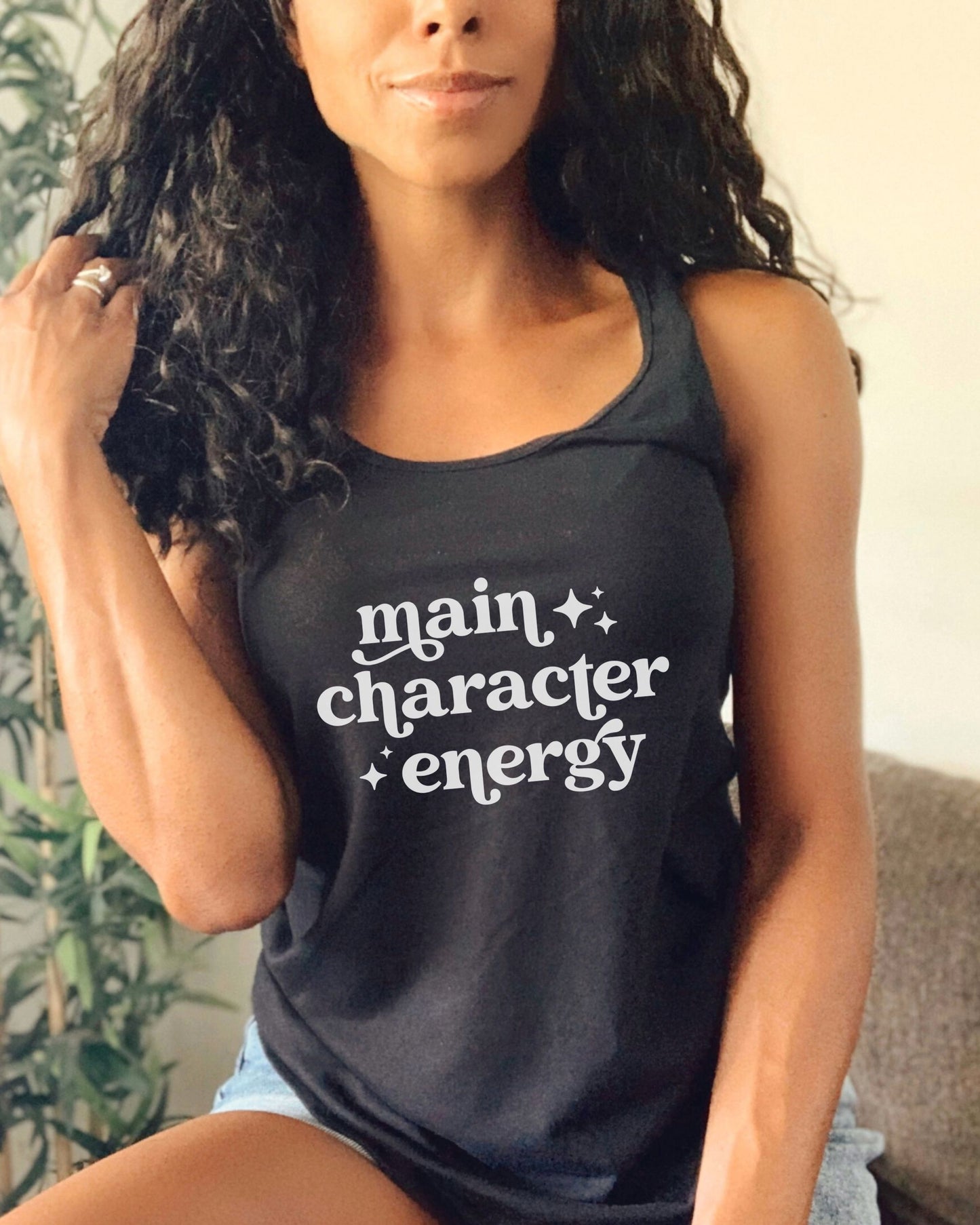 Woman wearing a black tank top with 'main character energy' text.