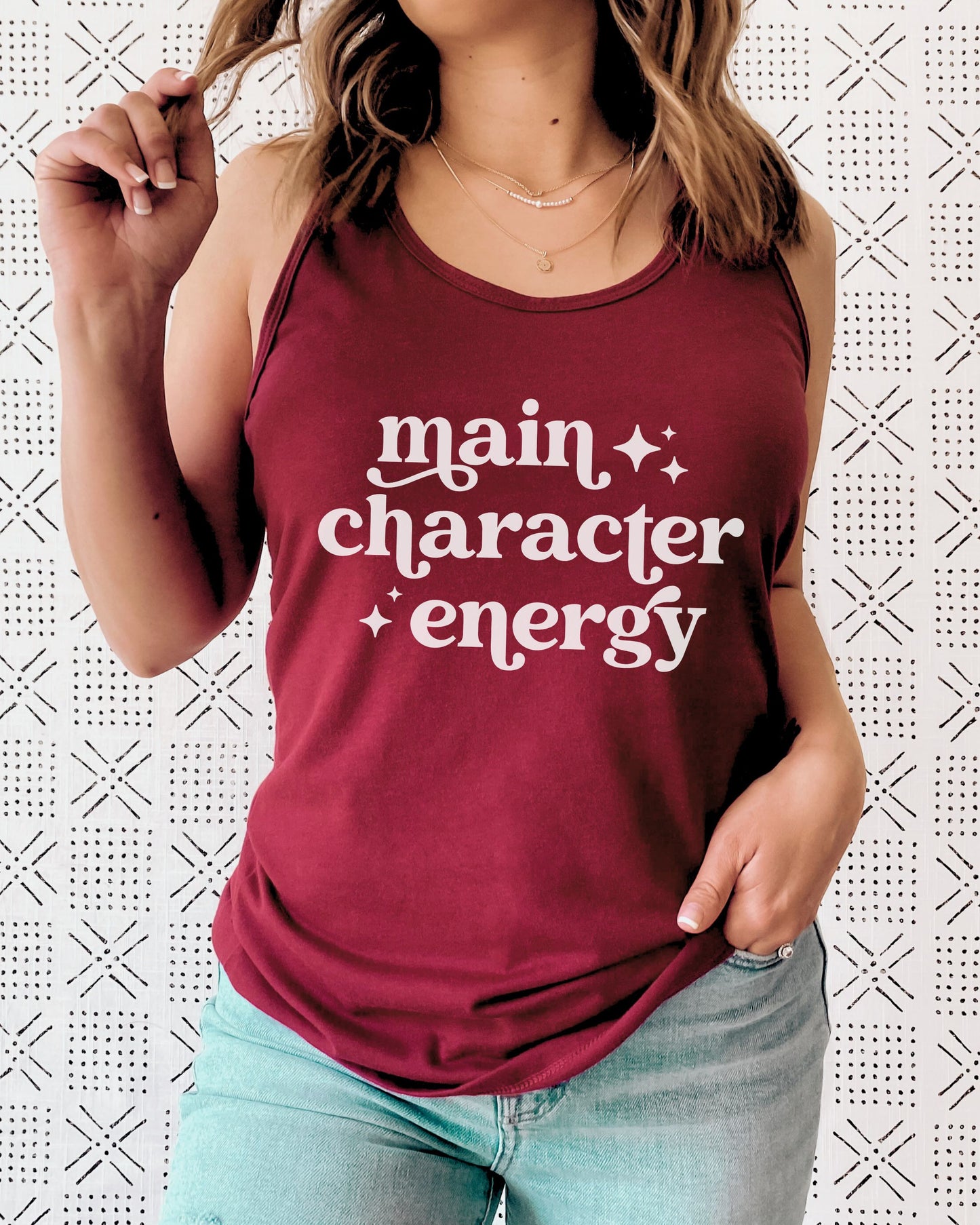 Person wearing a maroon tank top with 'main character energy' text on a patterned background