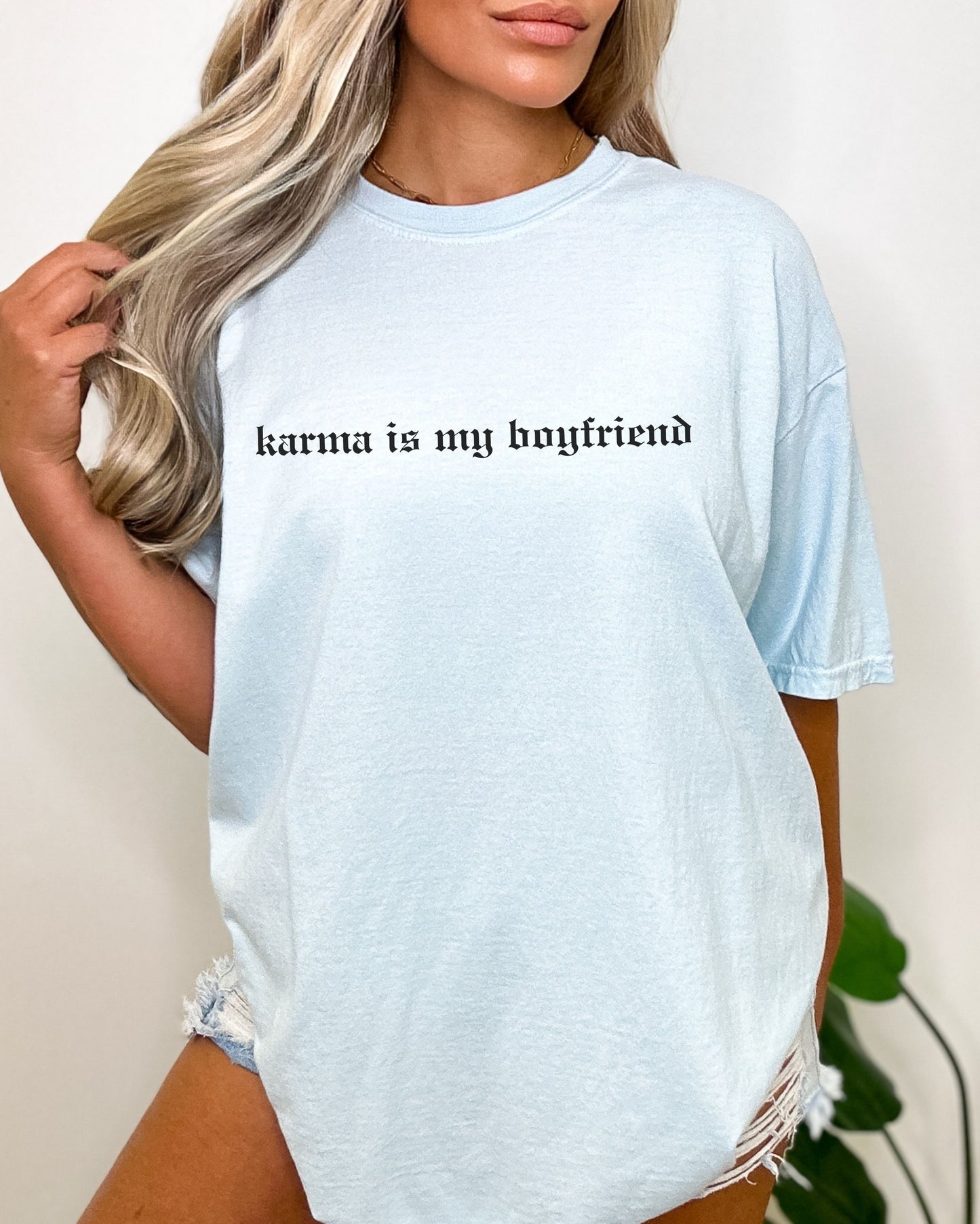 Light blue t-shirt with 'karma is my boyfriend' text worn by a person.