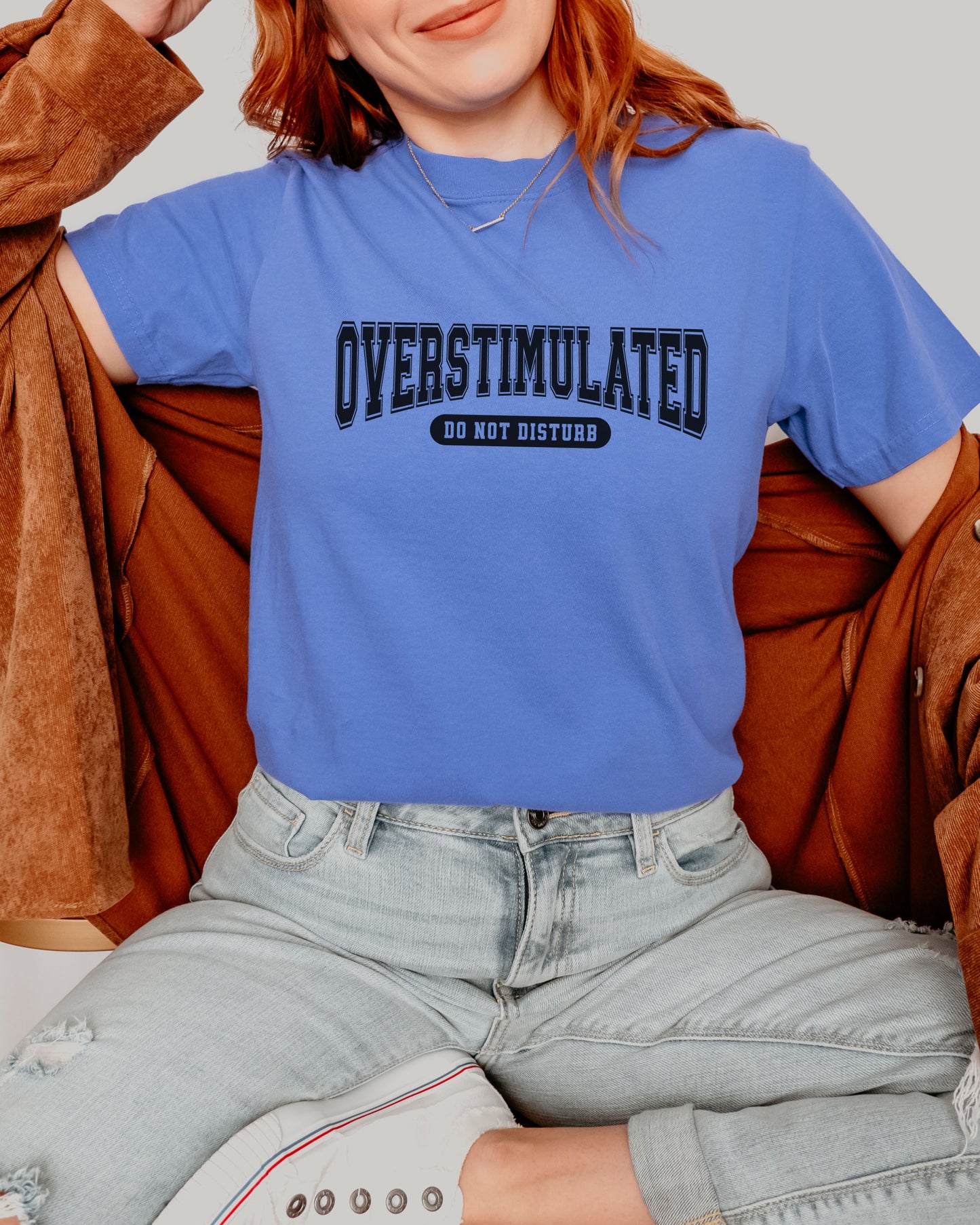 Person wearing a blue t-shirt with 'OVERSTIMULATED DO NOT DISTURB' text, sitting on a brown couch.