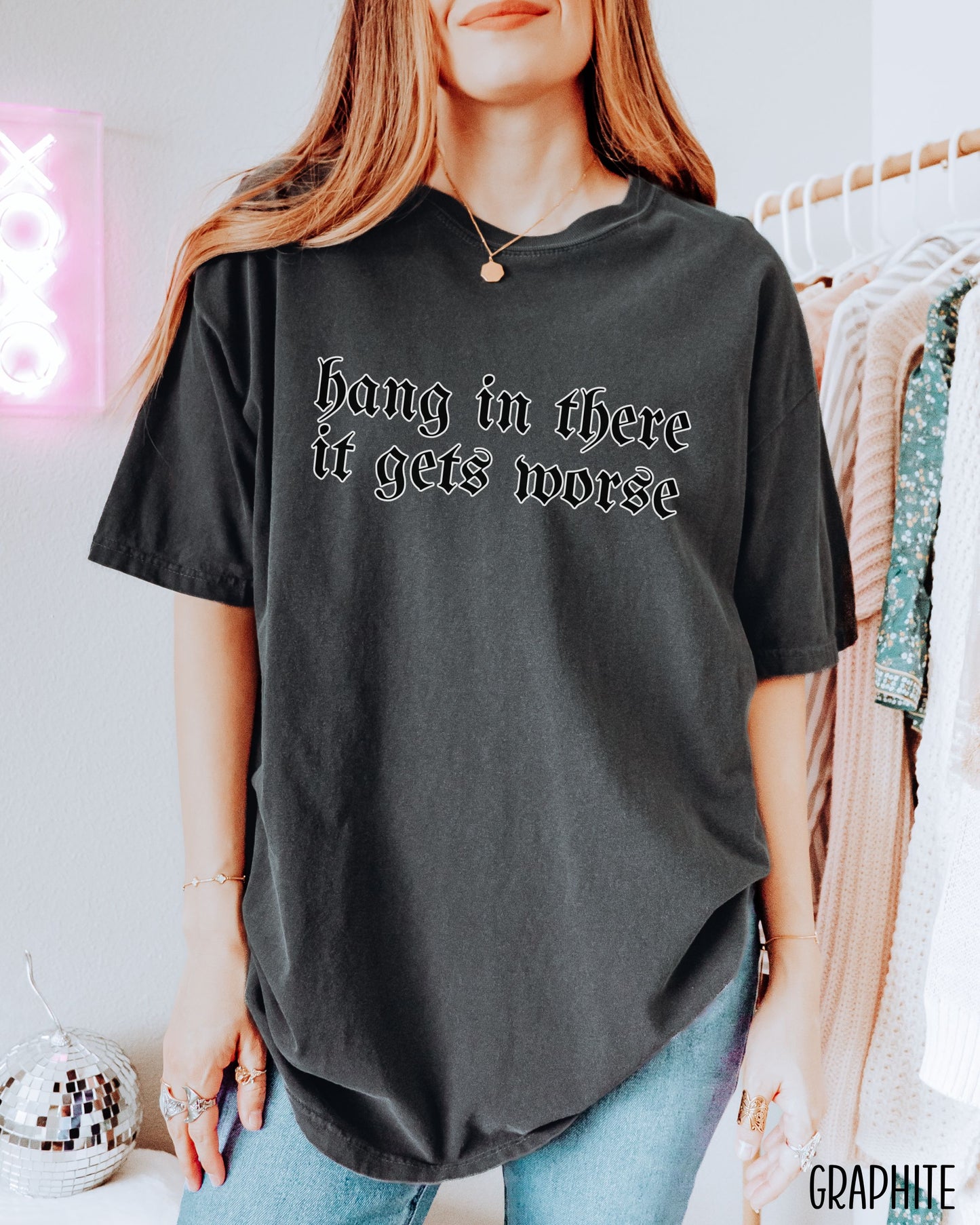 Person wearing a graphite t-shirt with 'hang in there it gets worse' text, standing in a room with clothing racks.