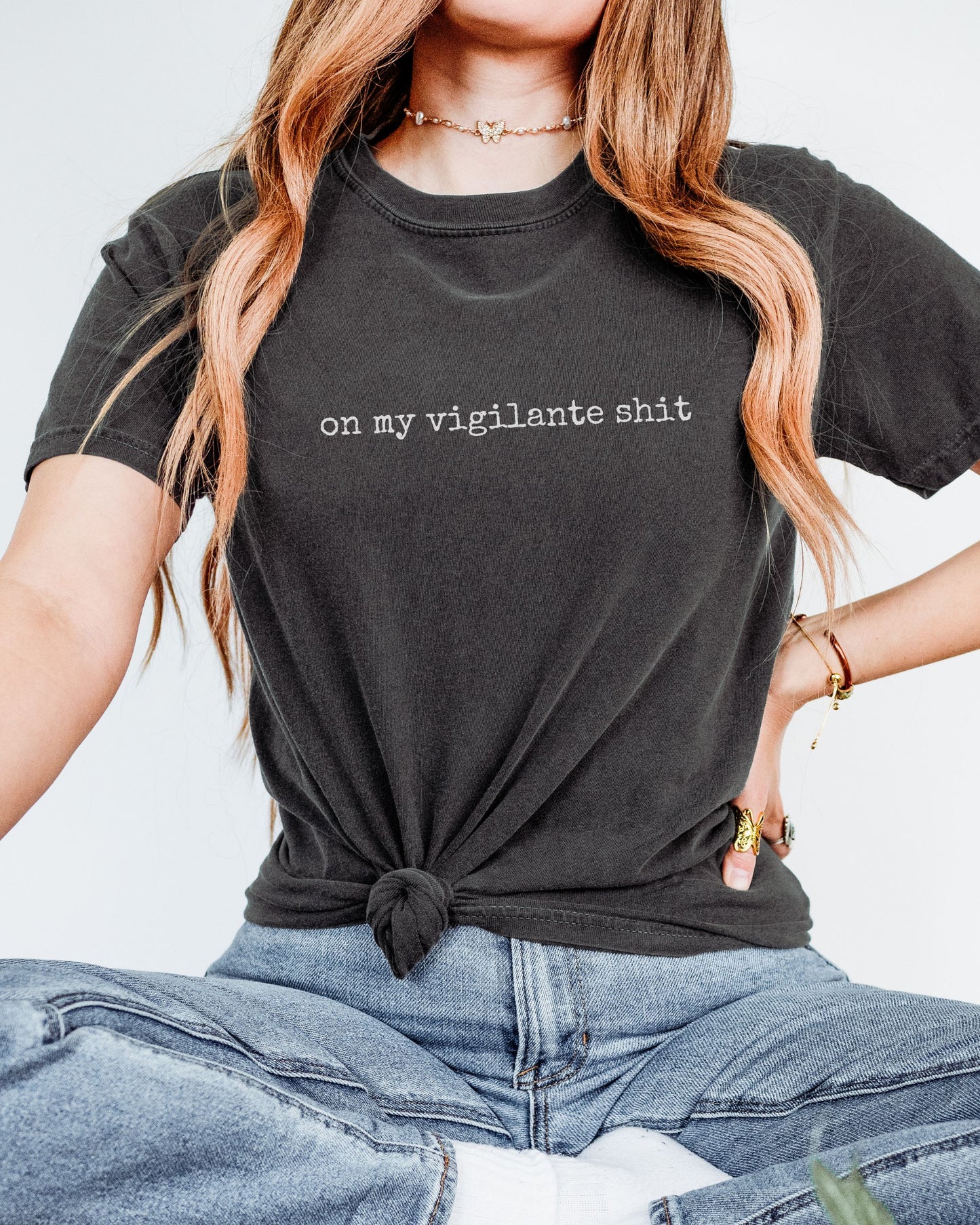 Person wearing a graphite t-shirt with on my vigilante shit text, sitting against a light background