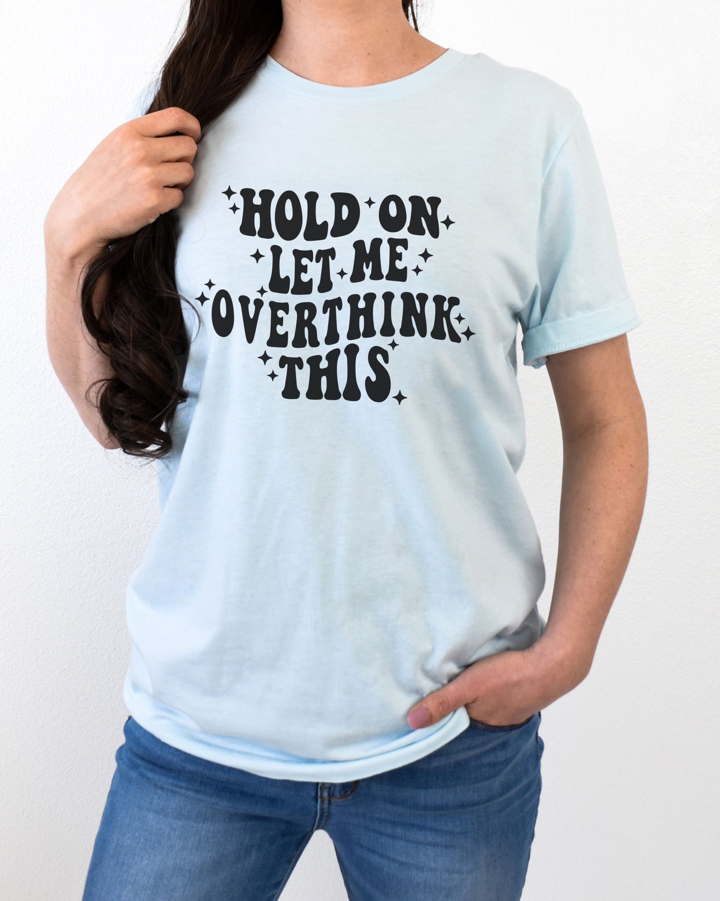 Person wearing a light blue t-shirt with text 'Hold on let me overthink this' on a plain background