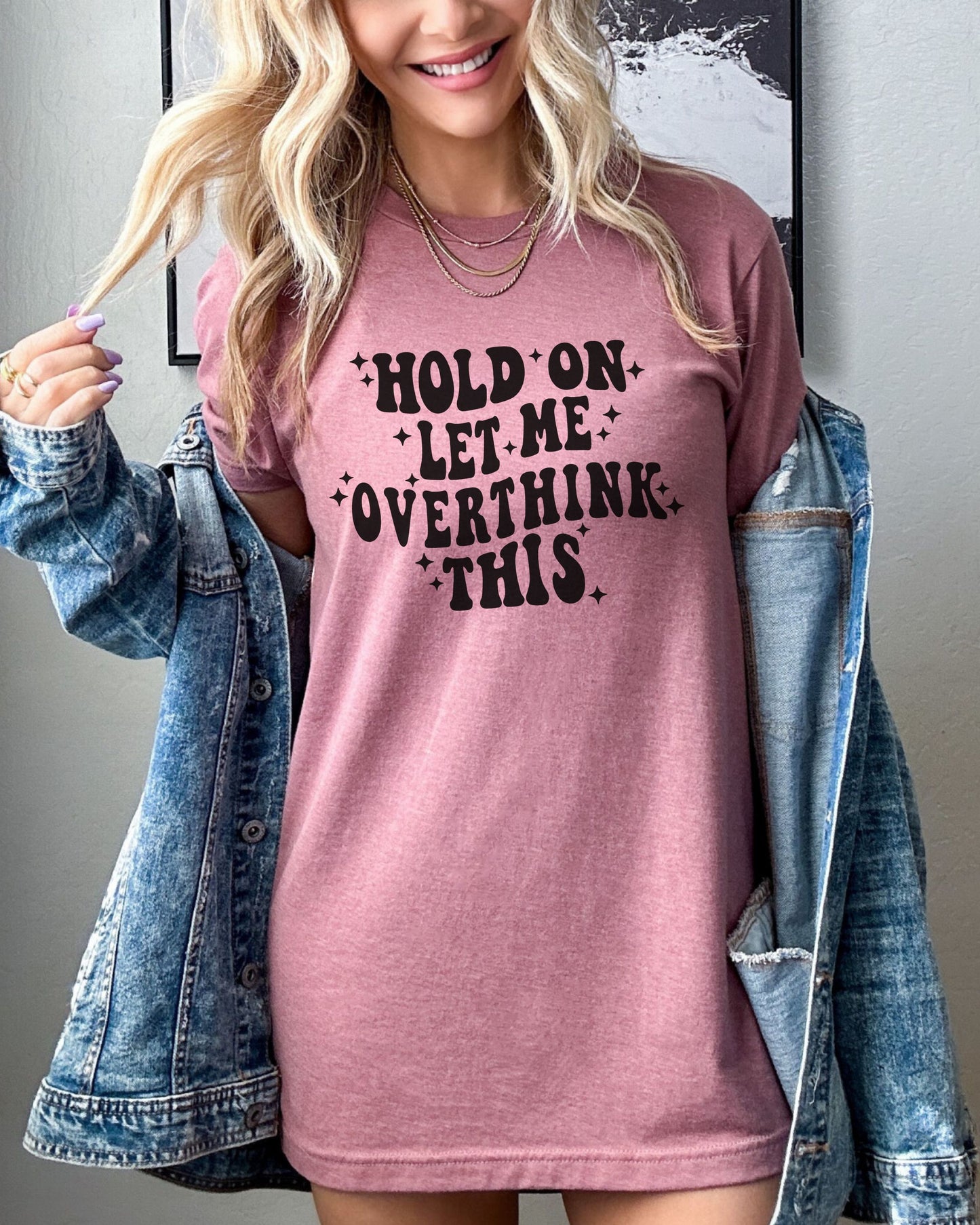 Person wearing a mauve t-shirt with text and a denim jacket.