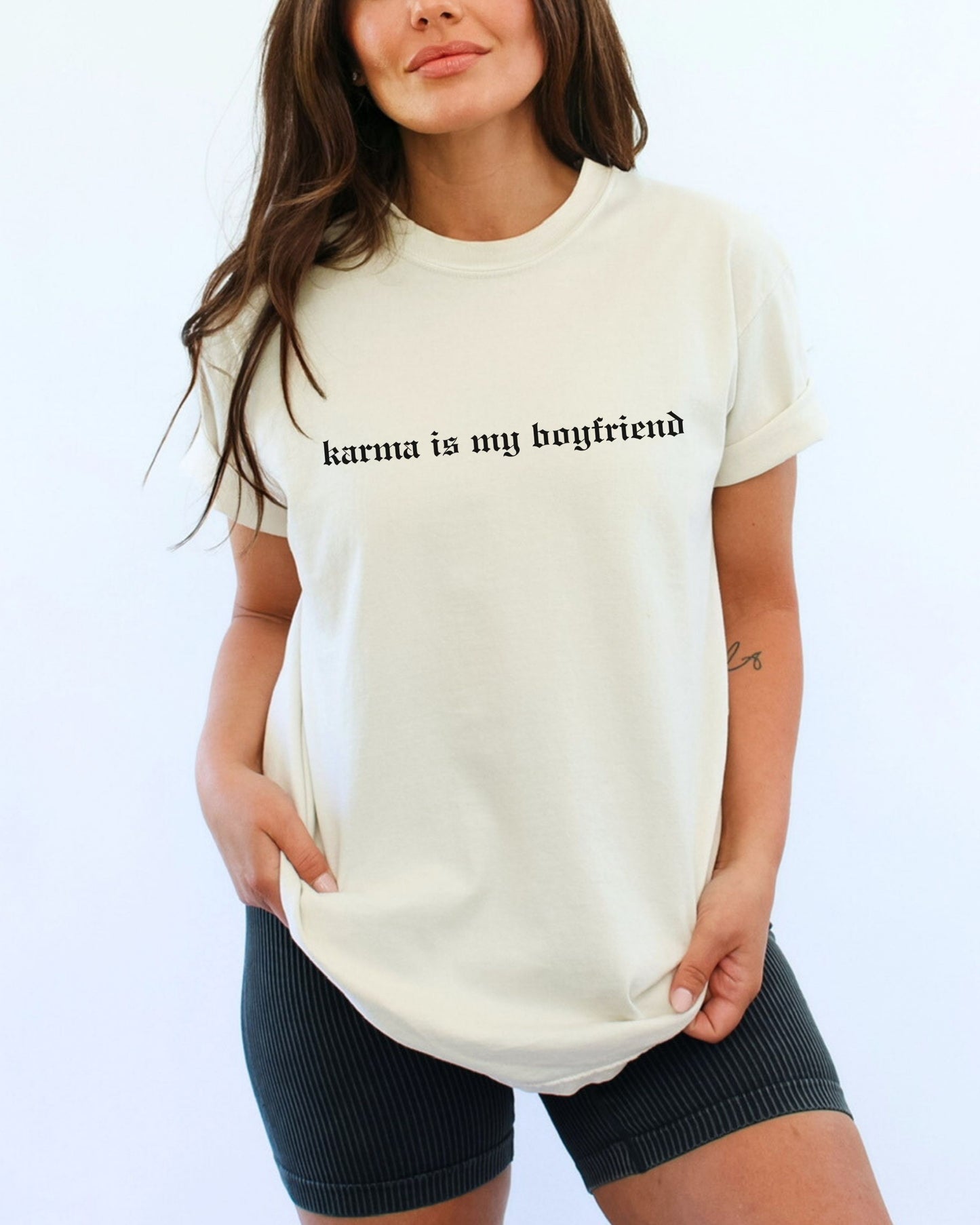 Woman wearing a white t-shirt with 'karma is my boyfriend' text on a plain background