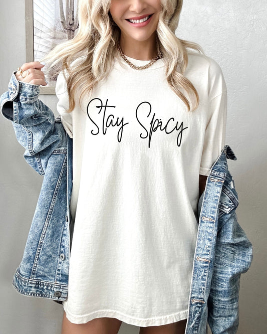 Woman wearing a white t-shirt with 'Stay Spicy' text, holding a denim jacket.