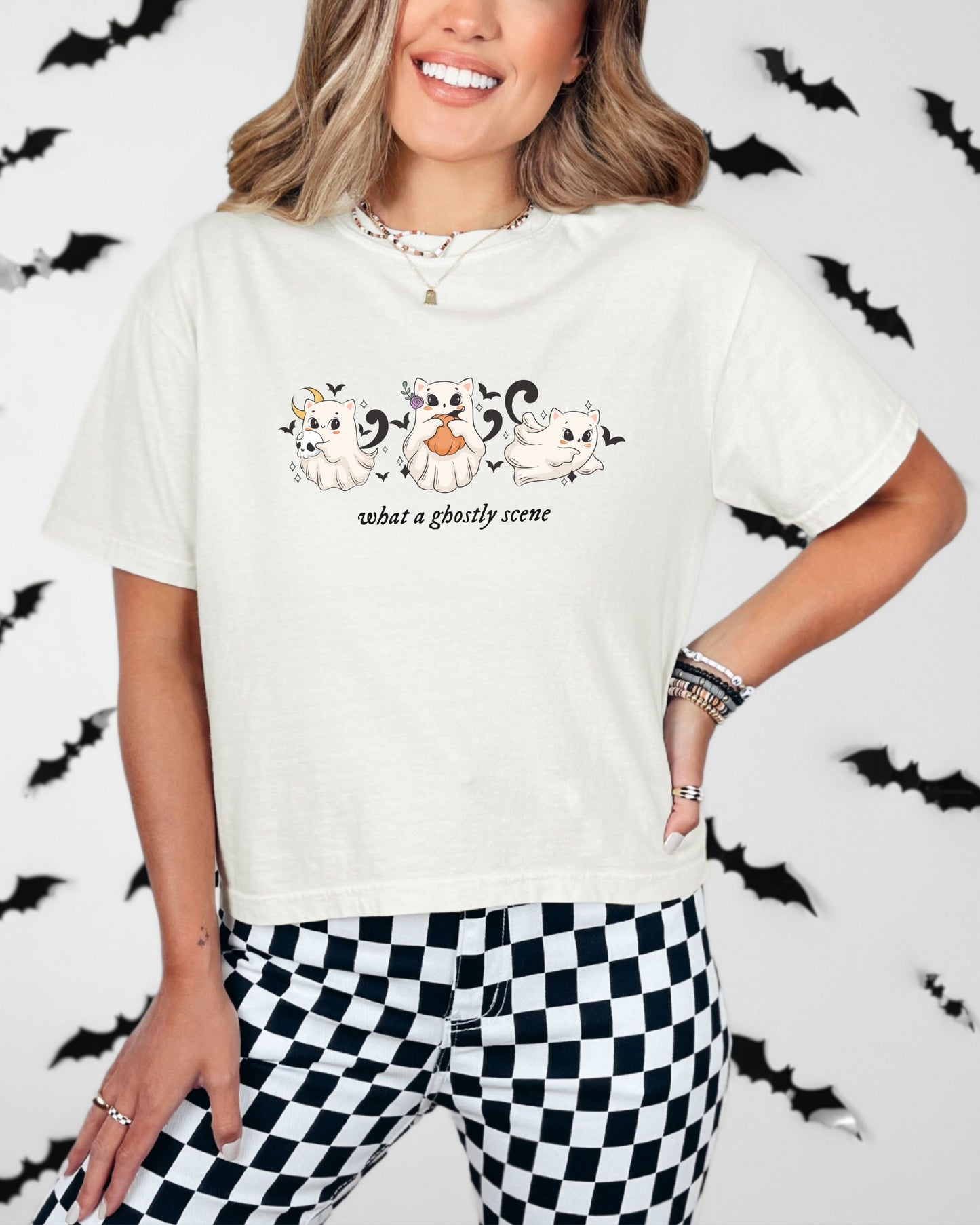 Person wearing a white t-shirt with a graphic design and black and white checkered pants on a Halloween-themed background.