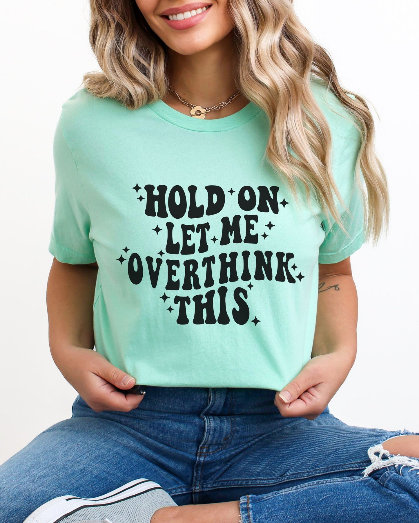 Person wearing a mint t-shirt with text 'Hold on let me overthink this' on a plain background