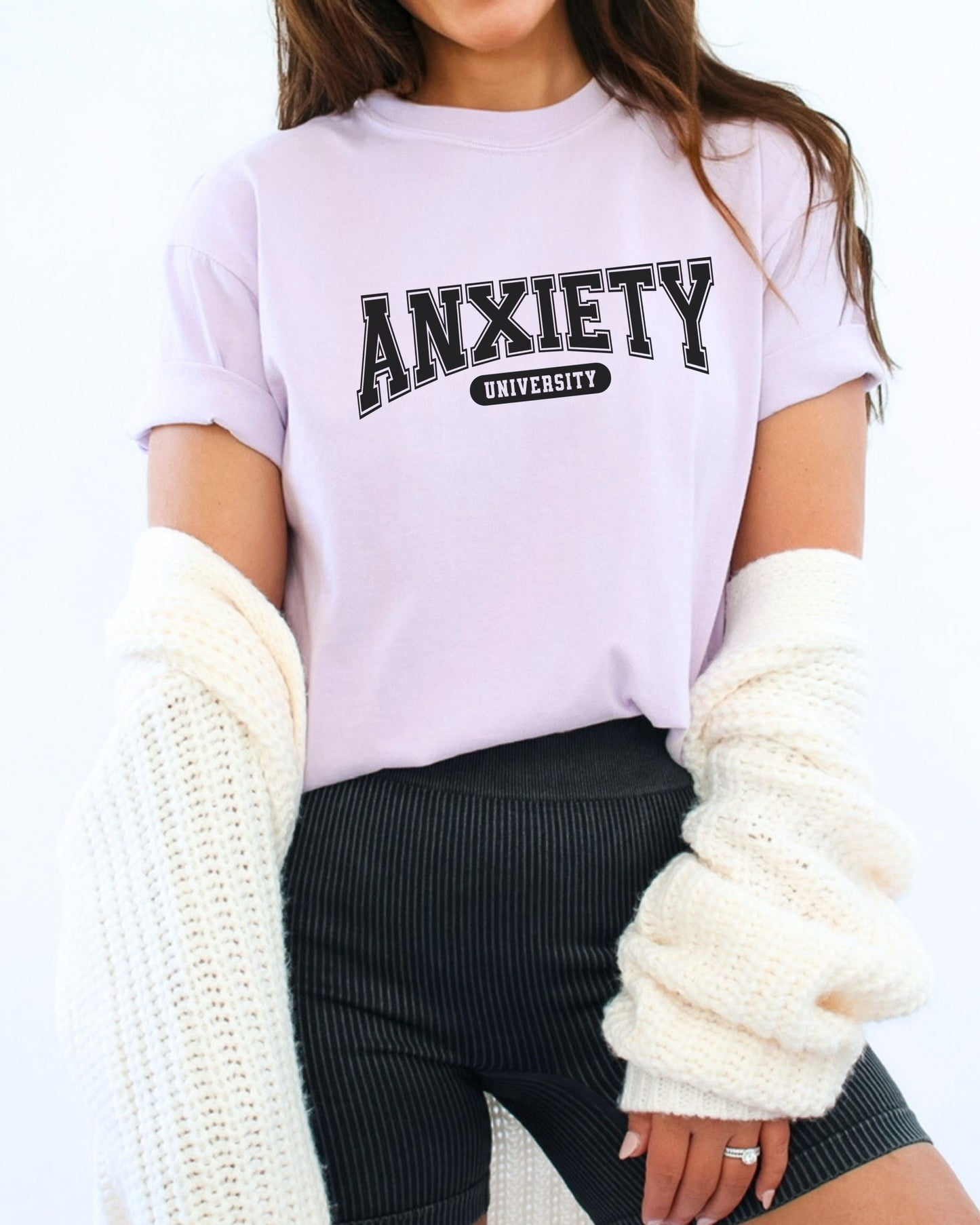 Person wearing a white t-shirt with 'ANXIETY UNIVERSITY' text, holding a white knit blanket.