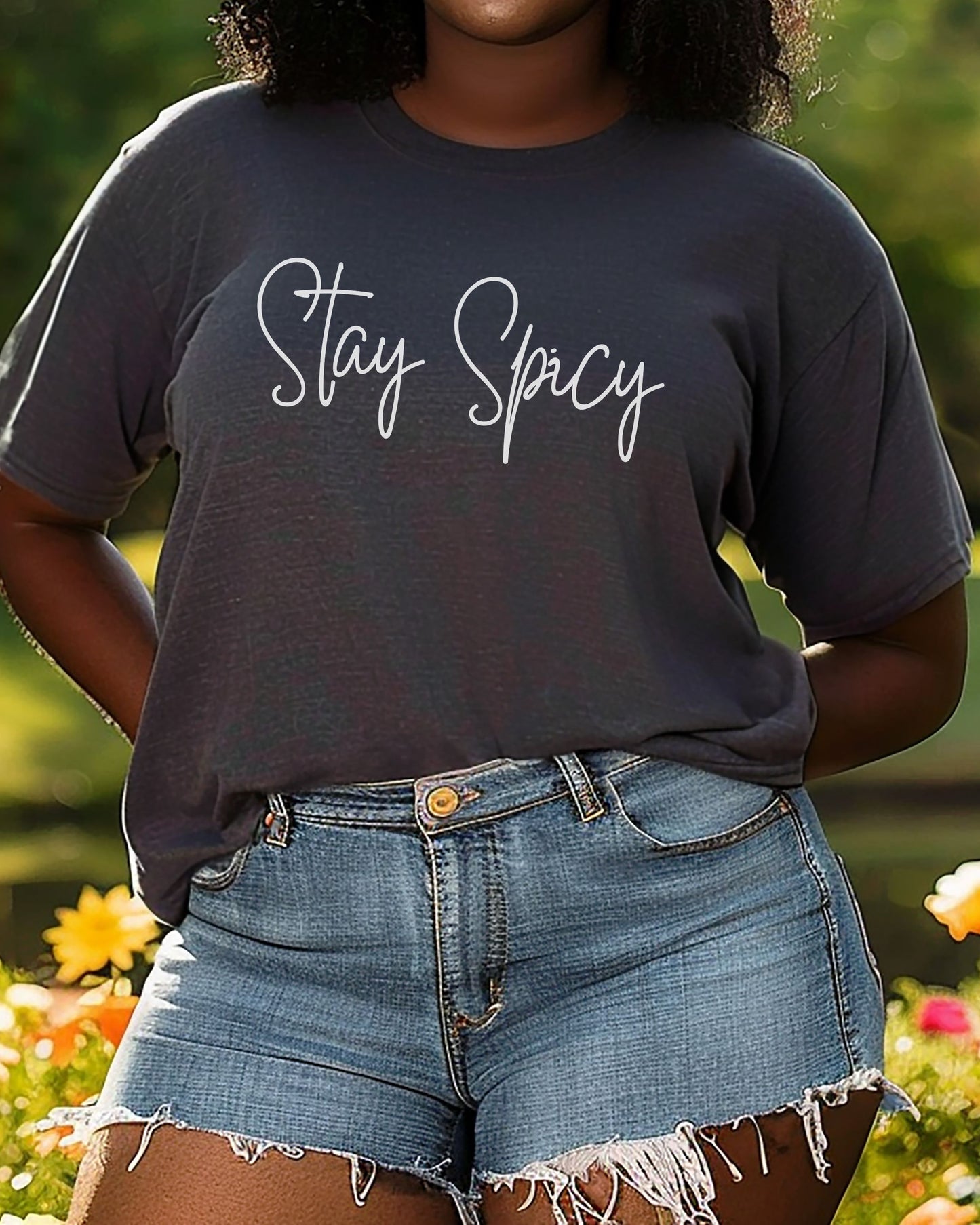 Person wearing a dark gray t-shirt with 'Stay Spicy' text and denim shorts outdoors.