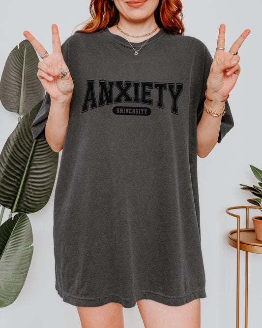 Person wearing a dark gray t-shirt with 'ANXIETY UNIVERSITY' text, making peace signs.