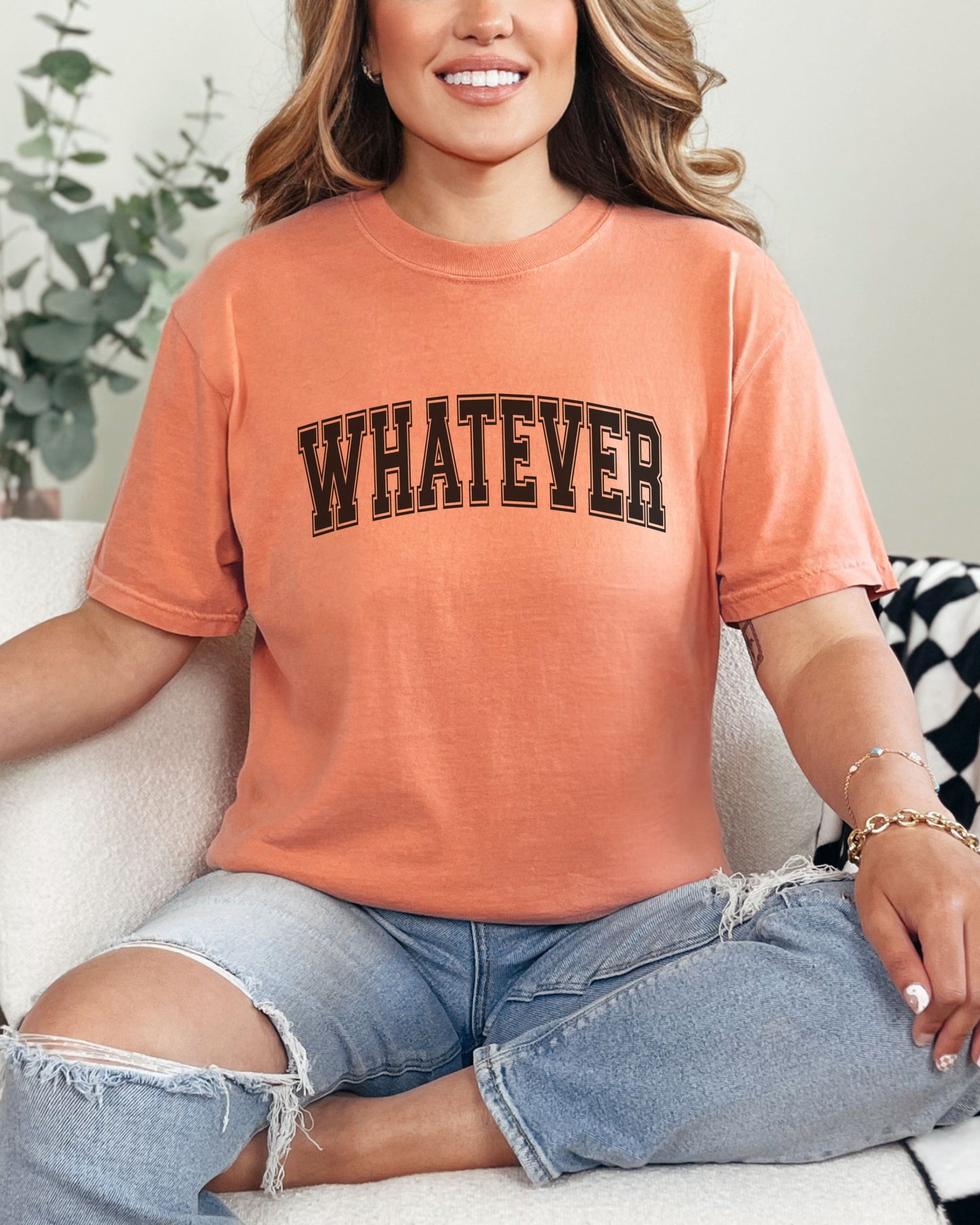 Person wearing an orange t-shirt with 'WHATEVER' text, sitting on a couch.