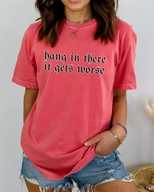 Person wearing a pink t-shirt with text 'hang in there it gets worse' against a plain background
