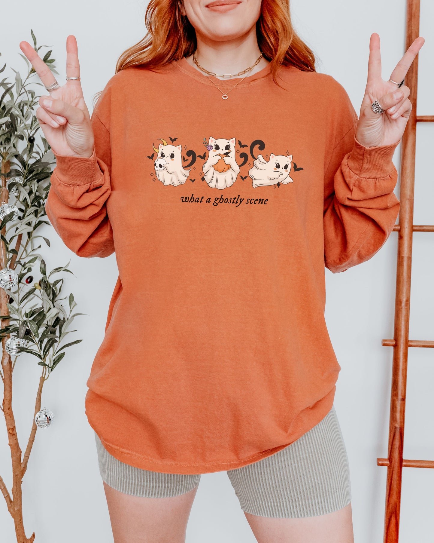 Person wearing an orange sweatshirt with cat graphics and text, making peace signs.