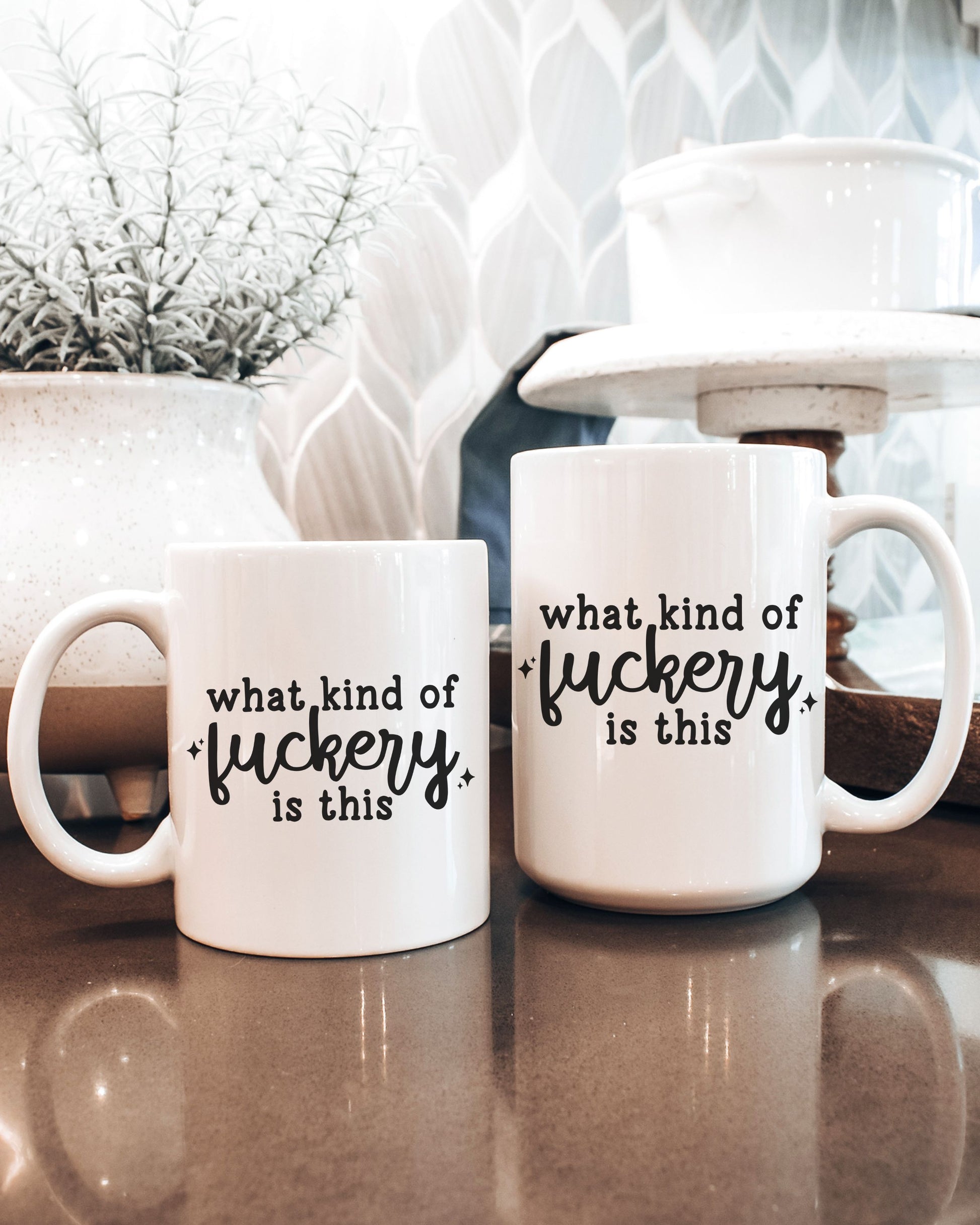 Two white mugs with black text on a reflective surface with decorative background