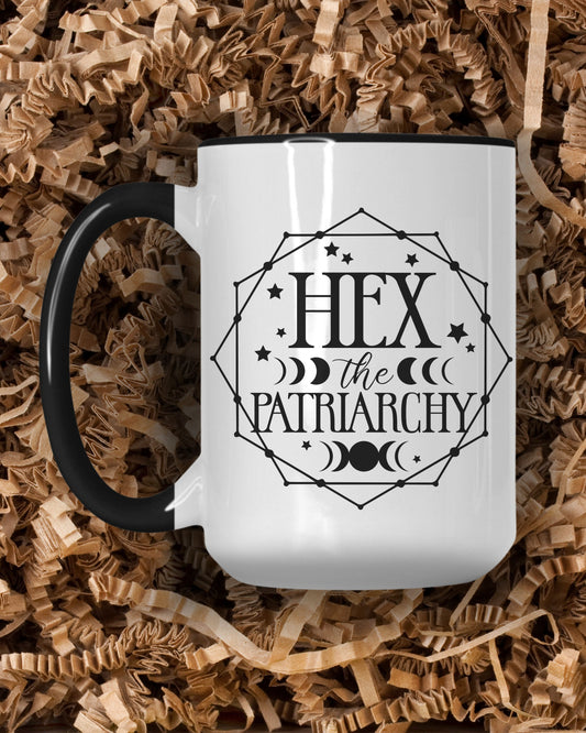 White mug with 'Hex the Patriarchy' design on a bed of wood shavings