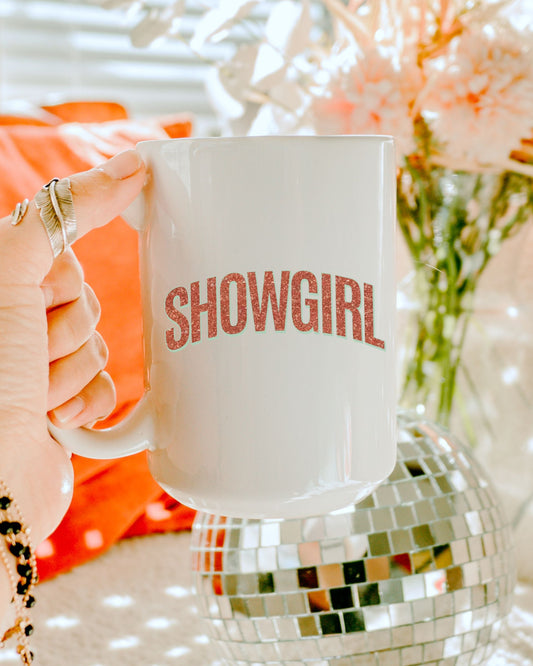 Person holding a 'SHOWGIRL' mug with a disco ball and flowers in the background