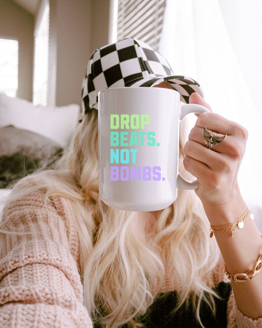 Person holding a mug with 'DROP BEATS, NOT BOMBS.' text, wearing a checkered hat indoors.