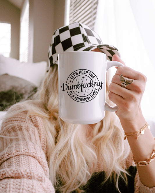 Person holding a mug with text, wearing a checkered hat and sweater.