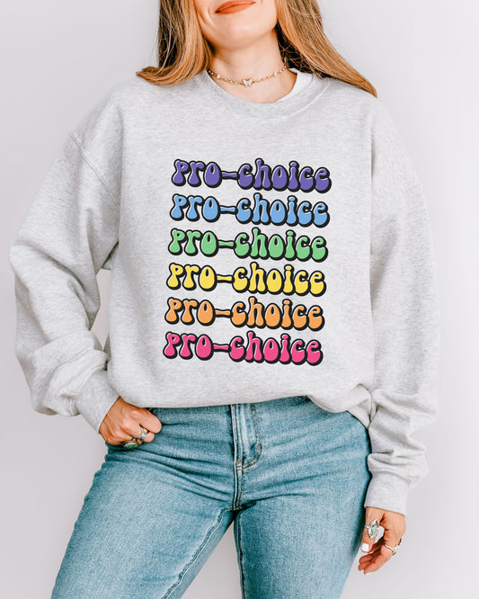 Person wearing a gray sweatshirt with 'PRO-CHOICE' in colorful letters on a plain background