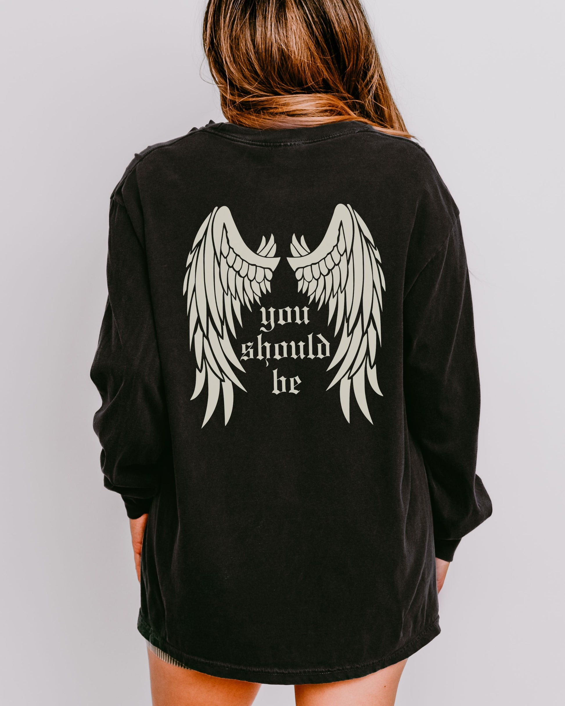Black long-sleeve shirt with angel wings and text on the back, worn by a person against a plain background.