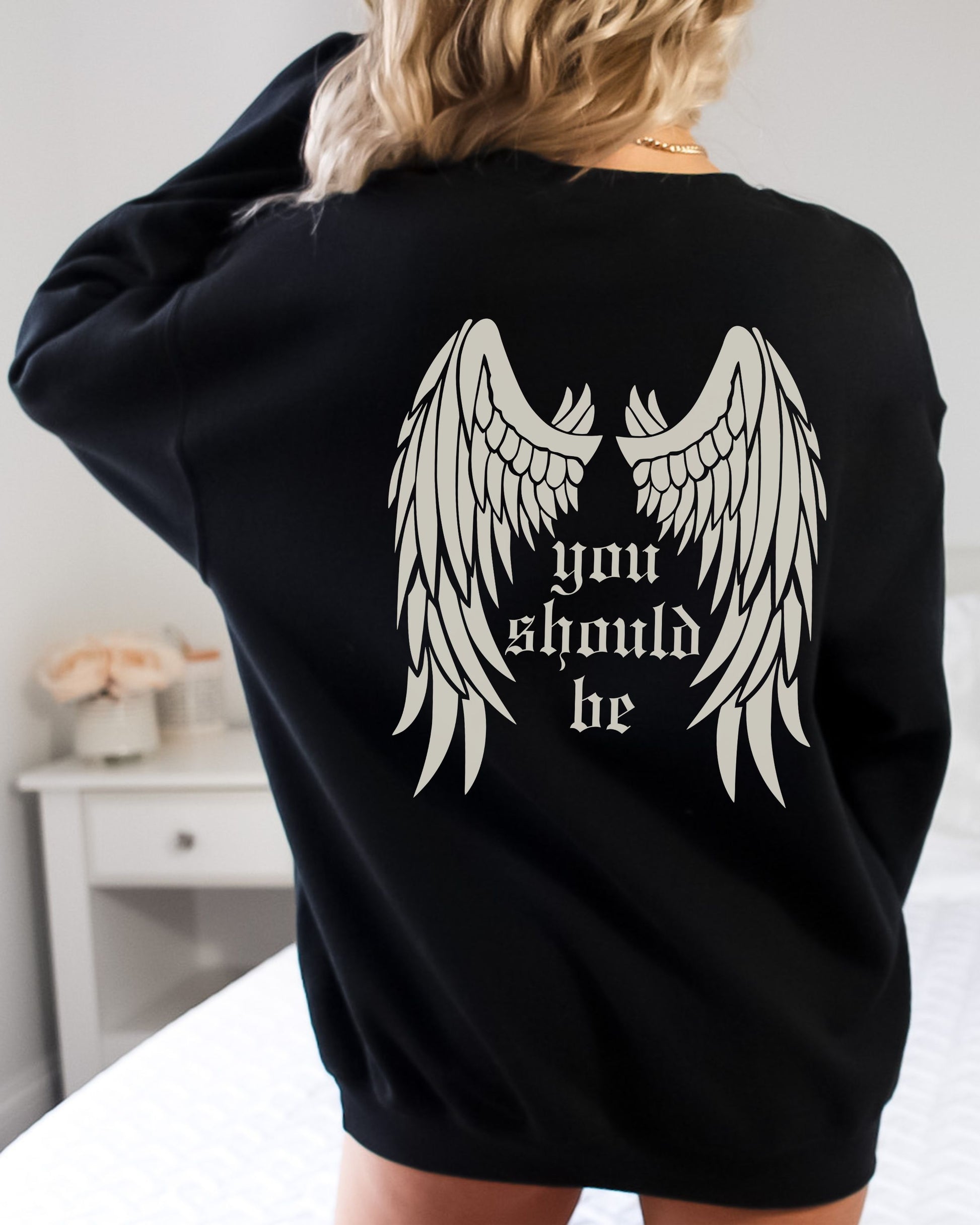 Black sweatshirt with angel wings and text on the back, worn by a person.