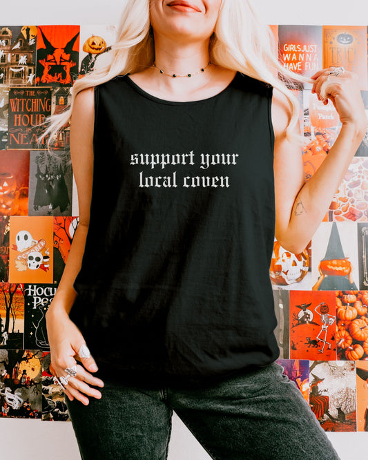 Person wearing a black tank top with 'support your local coven' text in front of Halloween-themed posters.