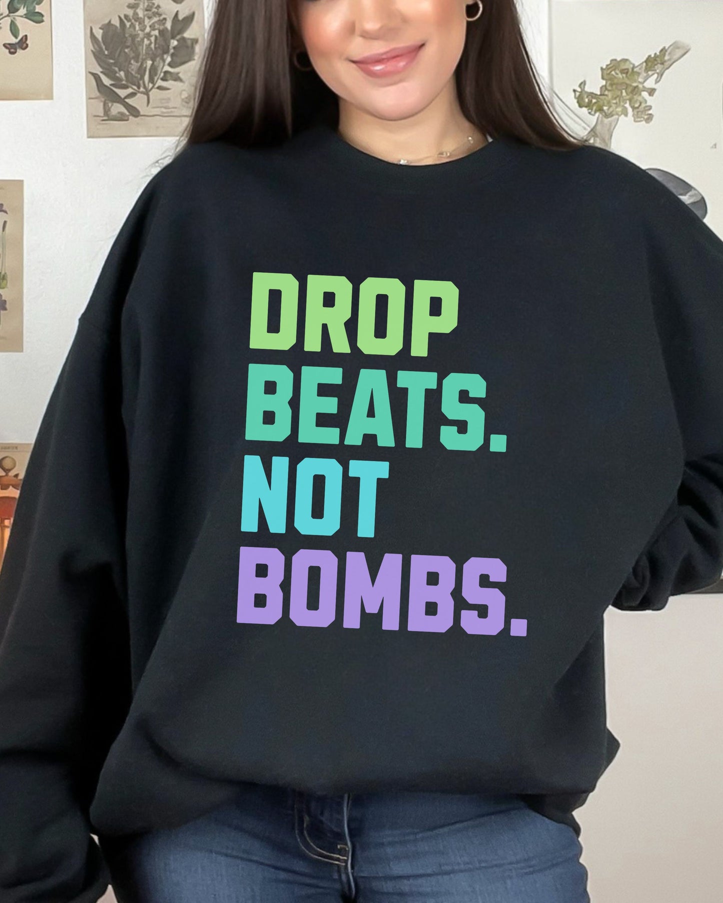Person wearing a black sweatshirt with colorful text 'DROP BEATS. NOT BOMBS.'
