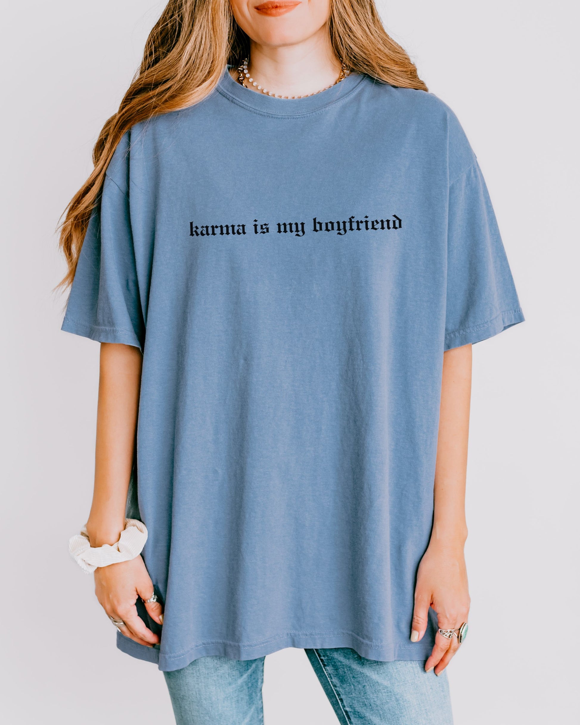 Person wearing a blue t-shirt with 'karma is my boyfriend' text on a plain background
