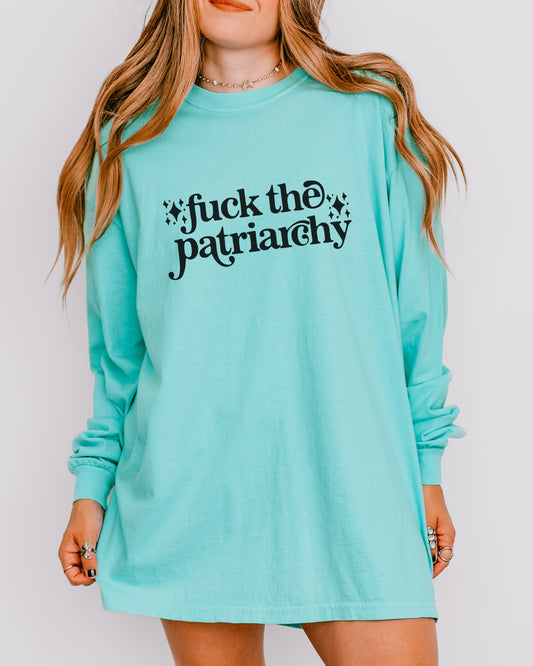 Person wearing a turquoise long-sleeve shirt with 'fuck the patriarchy' text on a plain background