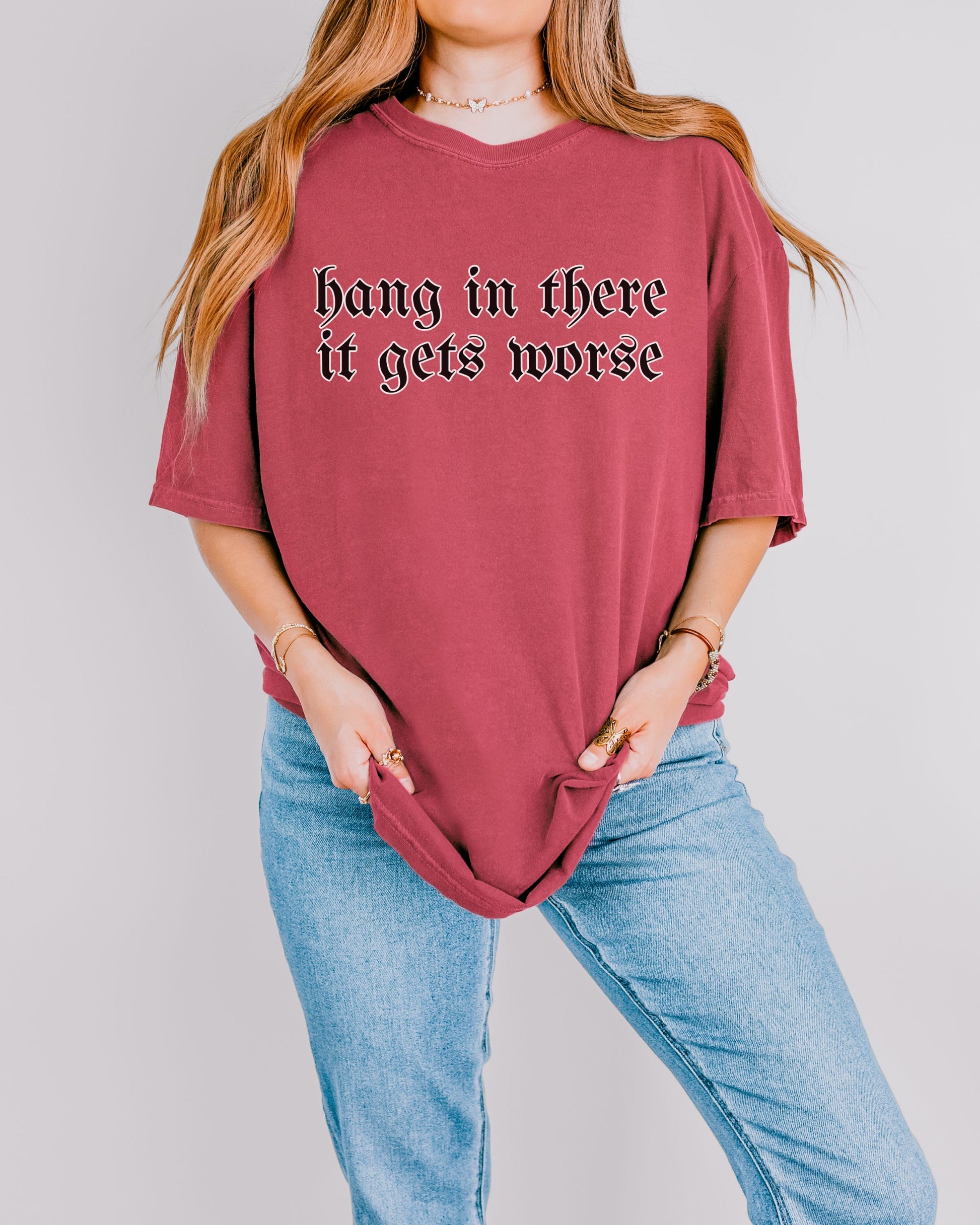 Person wearing a maroon t-shirt with text 'hang in there it gets worse' on a plain background