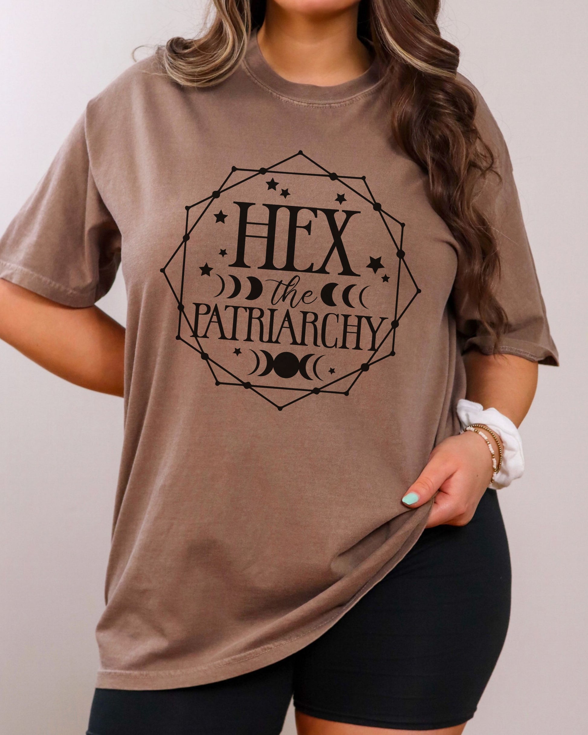 Person wearing a brown t-shirt with 'Hex the Patriarchy' text design.
