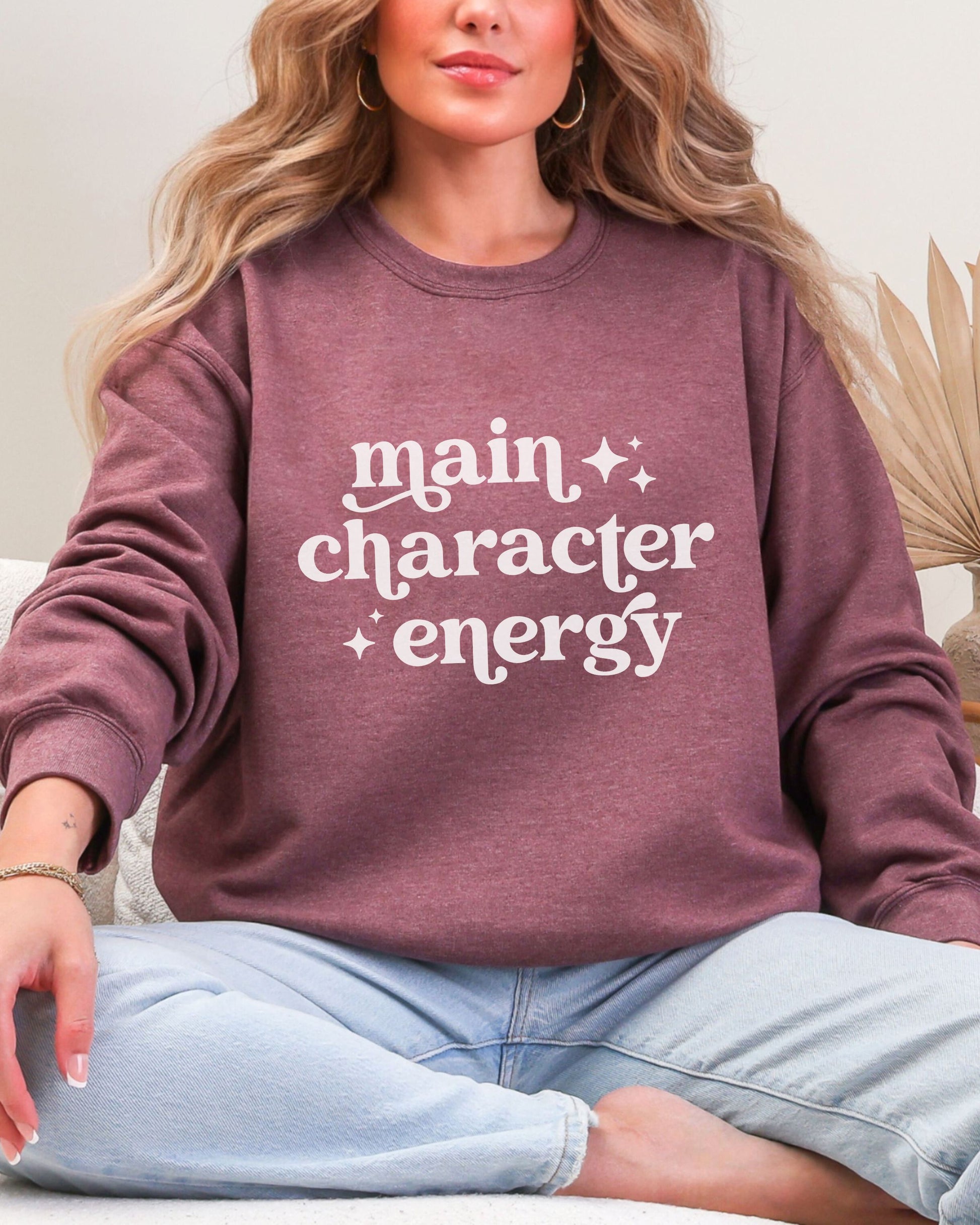 Person wearing a maroon sweatshirt with 'main character energy' text.