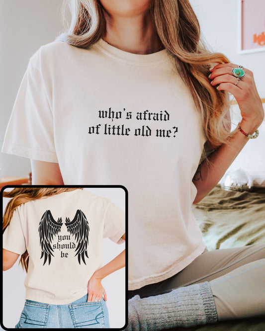 woman wearing comfort colors crop top in ivory with who’s afraid of little old me text on front and wings with you should be on back
